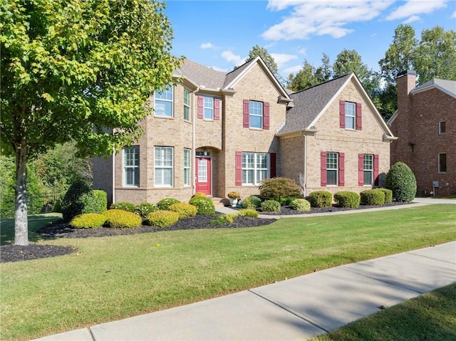 traditional home featuring a front lawn, brick siding, and roof with shingles