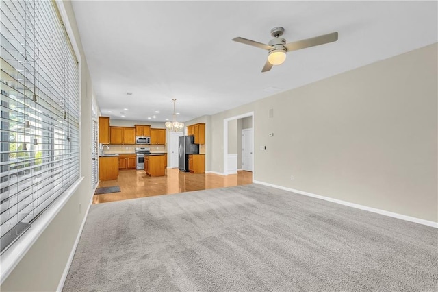 unfurnished living room with light carpet, a sink, ceiling fan with notable chandelier, recessed lighting, and baseboards