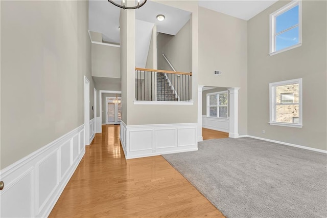 unfurnished living room featuring an inviting chandelier, a wealth of natural light, visible vents, and a towering ceiling