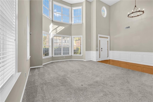 unfurnished living room with carpet floors, visible vents, an inviting chandelier, and a towering ceiling