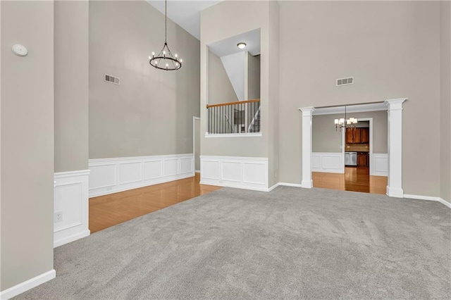 unfurnished living room with carpet floors, an inviting chandelier, visible vents, and a towering ceiling