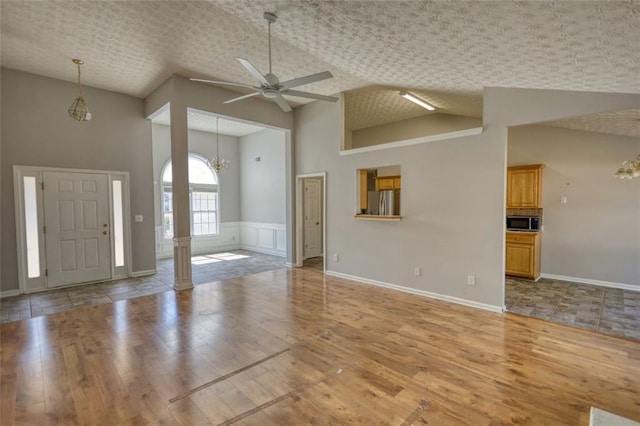 interior space featuring a textured ceiling, light wood-style flooring, high vaulted ceiling, and ceiling fan with notable chandelier