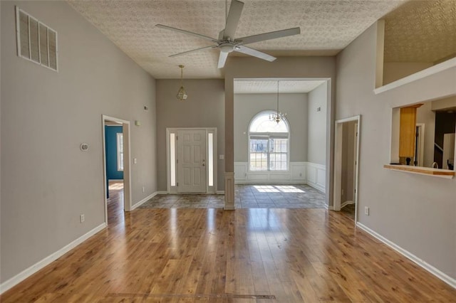 foyer featuring visible vents, a ceiling fan, a textured ceiling, hardwood / wood-style floors, and a towering ceiling