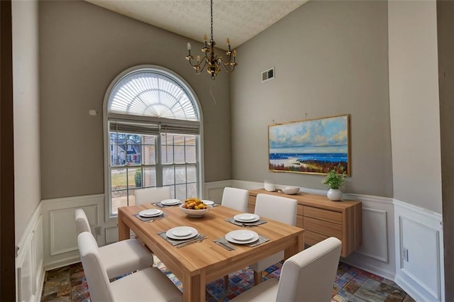 dining room with visible vents, a wainscoted wall, stone finish floor, a textured ceiling, and a chandelier