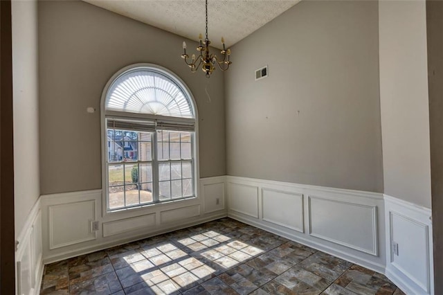 unfurnished dining area featuring visible vents, a wainscoted wall, an inviting chandelier, stone finish floor, and a textured ceiling