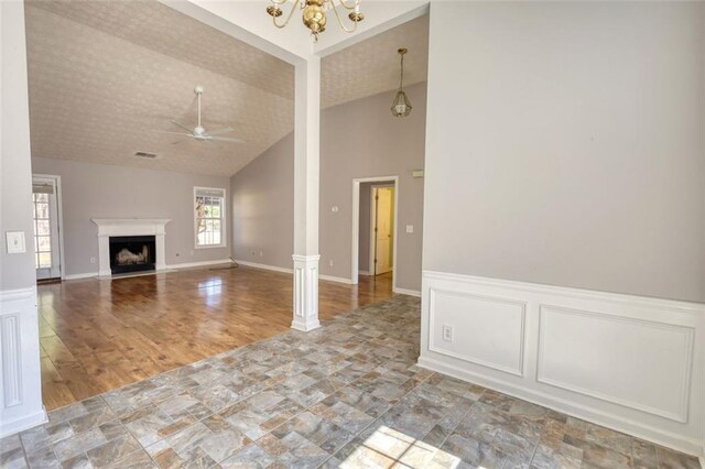 unfurnished living room featuring wainscoting, ceiling fan with notable chandelier, a fireplace, and ornate columns