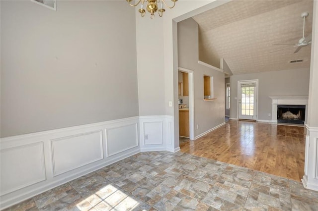 unfurnished living room with visible vents, ceiling fan with notable chandelier, a fireplace, a decorative wall, and vaulted ceiling