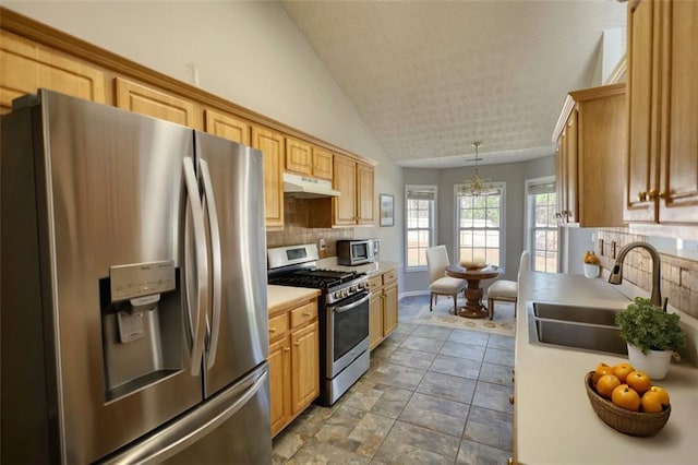 kitchen featuring a sink, decorative backsplash, vaulted ceiling, under cabinet range hood, and appliances with stainless steel finishes