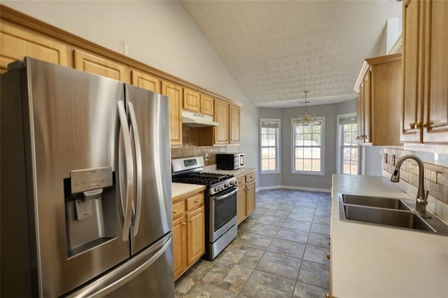 kitchen with a sink, under cabinet range hood, backsplash, appliances with stainless steel finishes, and vaulted ceiling