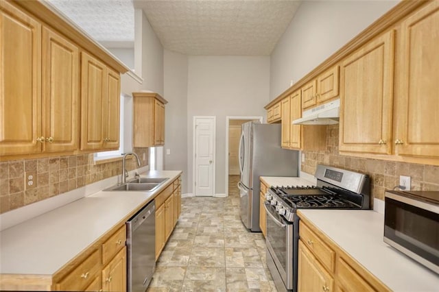 kitchen featuring light brown cabinetry, a sink, light countertops, under cabinet range hood, and appliances with stainless steel finishes