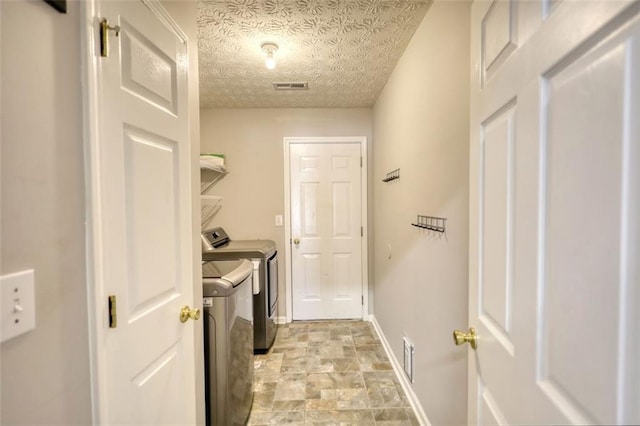 clothes washing area featuring washing machine and clothes dryer, visible vents, baseboards, laundry area, and stone finish floor