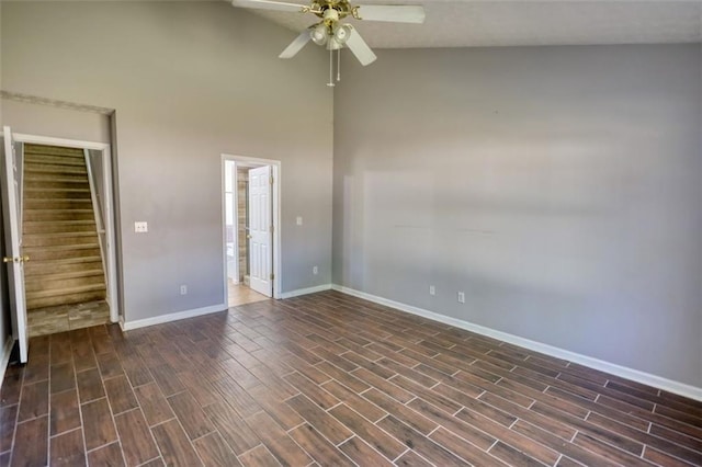 spare room with dark wood-type flooring, ceiling fan, baseboards, stairway, and high vaulted ceiling