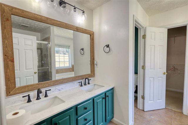 bathroom with a textured ceiling, tile patterned floors, a stall shower, and a sink