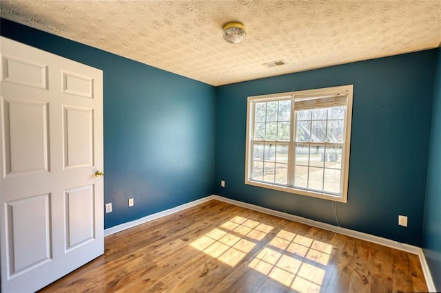 spare room featuring visible vents, a textured ceiling, baseboards, and hardwood / wood-style flooring