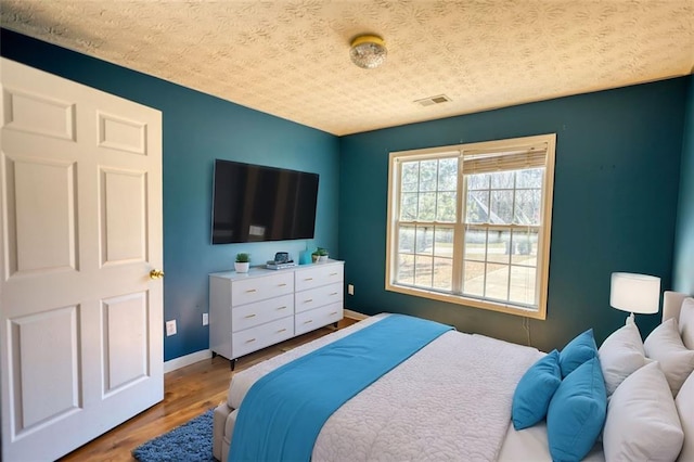 bedroom featuring a textured ceiling, wood finished floors, visible vents, and baseboards