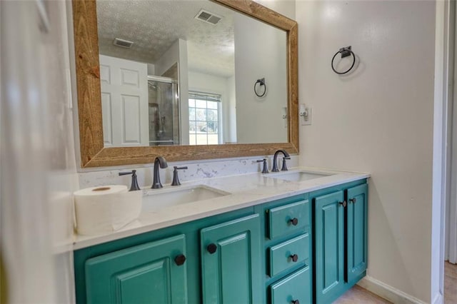 full bath with visible vents, a stall shower, a textured ceiling, and a sink