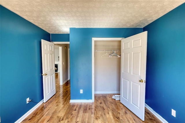 unfurnished bedroom with a textured ceiling, wood finished floors, a closet, and baseboards