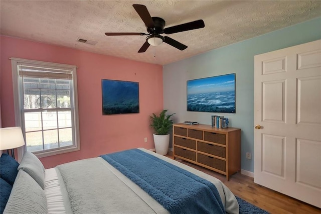 bedroom featuring visible vents, baseboards, wood finished floors, a textured ceiling, and a ceiling fan