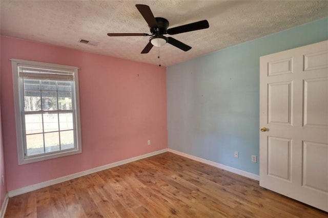 unfurnished room featuring a ceiling fan, wood finished floors, visible vents, baseboards, and a textured ceiling