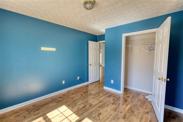 unfurnished bedroom with a closet, a textured ceiling, baseboards, and wood finished floors