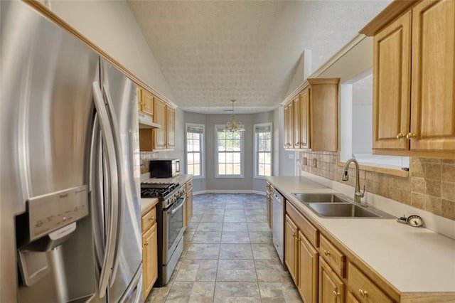 kitchen featuring under cabinet range hood, light countertops, decorative backsplash, stainless steel appliances, and a sink