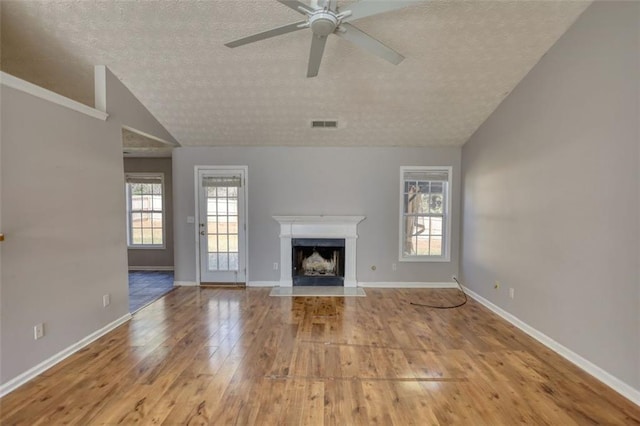 unfurnished living room with a fireplace with flush hearth, lofted ceiling, a textured ceiling, hardwood / wood-style floors, and baseboards