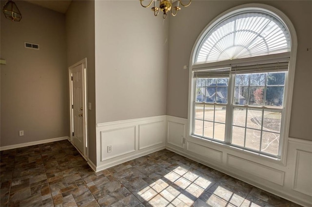 unfurnished dining area with visible vents, an inviting chandelier, stone finish floor, wainscoting, and a decorative wall