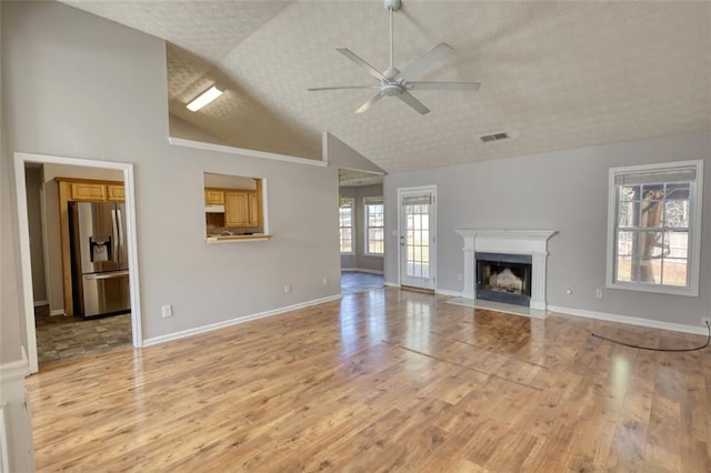 unfurnished living room with a ceiling fan, a textured ceiling, a high end fireplace, light wood finished floors, and baseboards