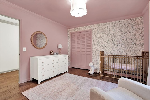 bedroom with a closet, dark wood-type flooring, a nursery area, and ornamental molding