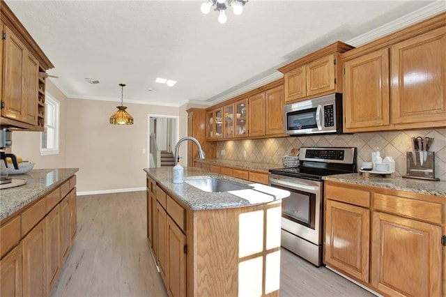 kitchen with light hardwood / wood-style floors, pendant lighting, sink, an island with sink, and stainless steel appliances