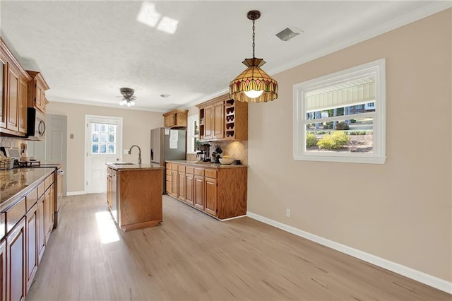 kitchen featuring sink, light hardwood / wood-style flooring, hanging light fixtures, appliances with stainless steel finishes, and an island with sink