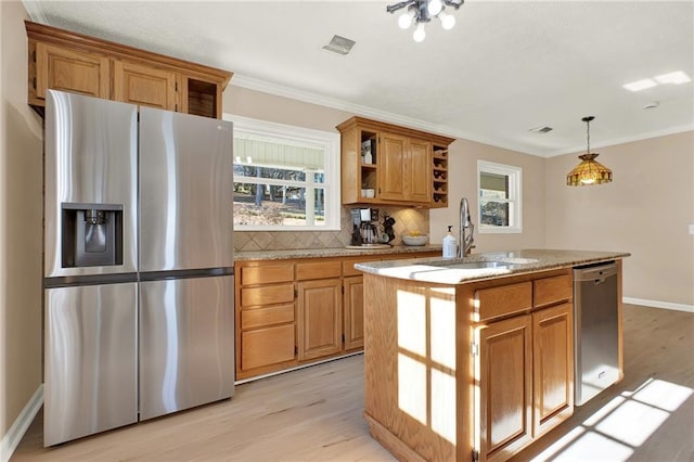 kitchen featuring appliances with stainless steel finishes, an island with sink, sink, hanging light fixtures, and light wood-type flooring