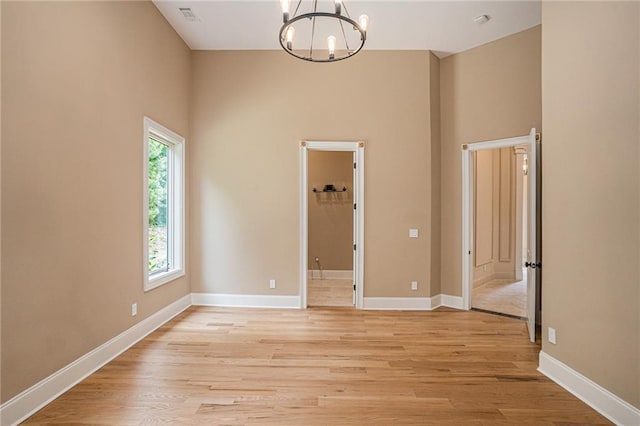 empty room with a towering ceiling, an inviting chandelier, and light wood-type flooring