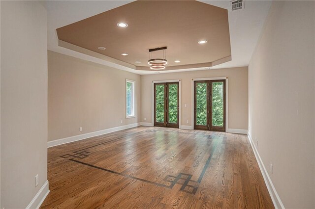 empty room with wood-type flooring, french doors, a chandelier, and a tray ceiling