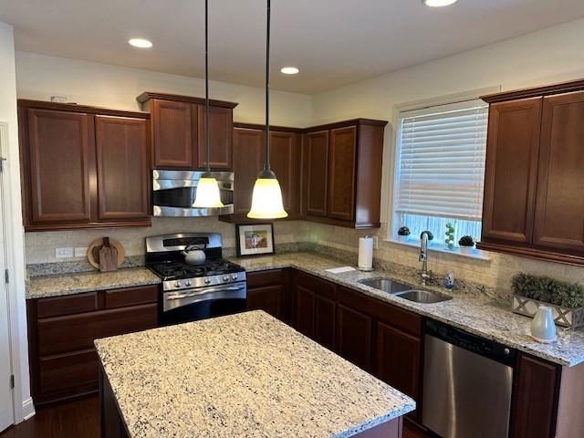 kitchen featuring decorative light fixtures, stainless steel appliances, backsplash, a sink, and light stone countertops