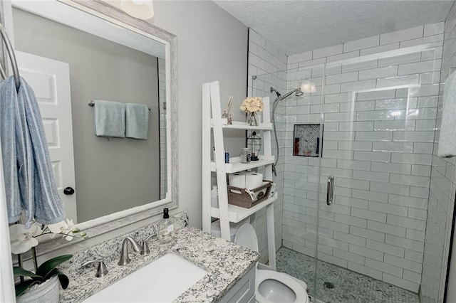 bathroom featuring a textured ceiling, a shower with door, vanity, and toilet