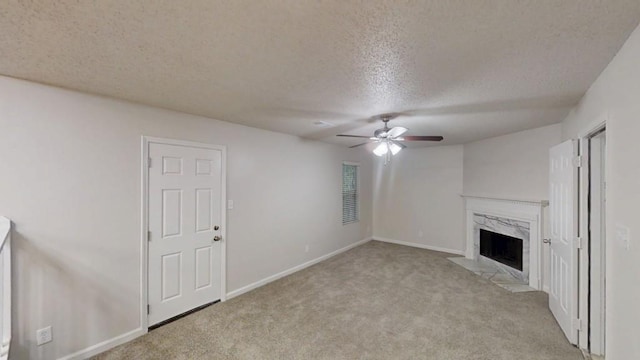 unfurnished living room with a textured ceiling, a ceiling fan, carpet floors, a high end fireplace, and baseboards