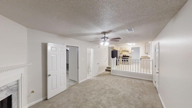 unfurnished living room with a premium fireplace, a ceiling fan, light colored carpet, a textured ceiling, and baseboards