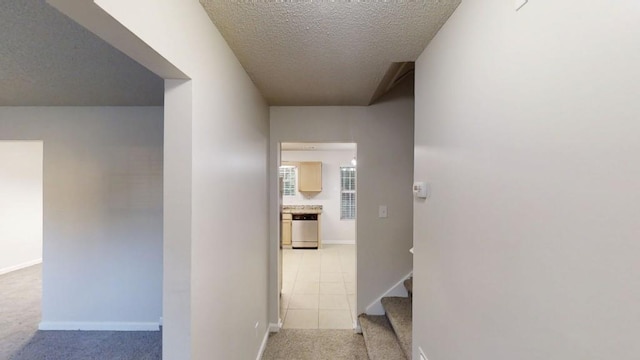 hall featuring a textured ceiling, light colored carpet, and baseboards