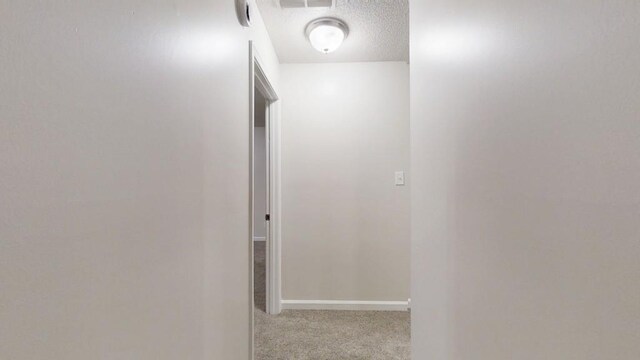 hallway featuring carpet, a textured ceiling, and baseboards