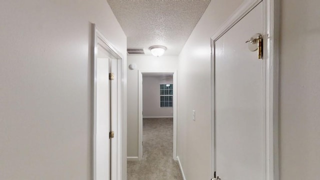 corridor featuring a textured ceiling, baseboards, and light carpet