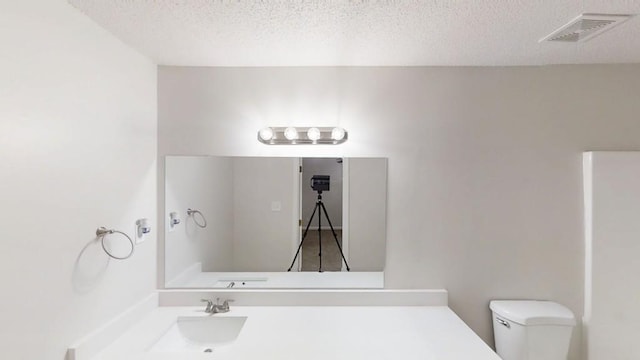 bathroom with toilet, a textured ceiling, and a sink