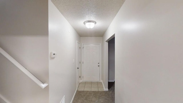 hallway with a textured ceiling, carpet, and baseboards