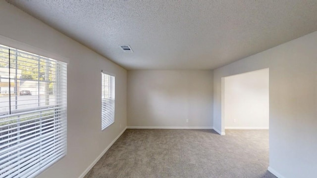 carpeted empty room with a textured ceiling and baseboards