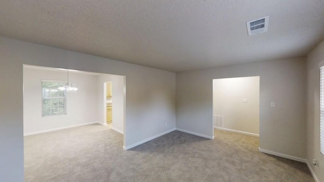 spare room featuring carpet, a chandelier, baseboards, and a textured ceiling