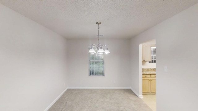 empty room featuring a chandelier, light carpet, a textured ceiling, and baseboards