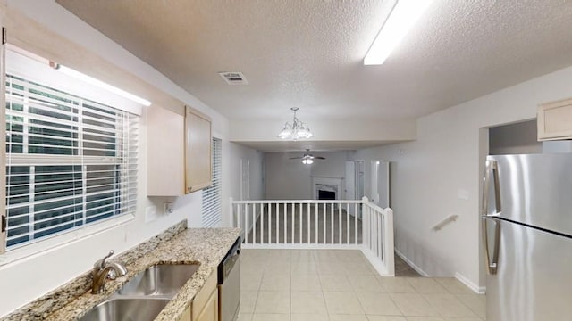 kitchen with stainless steel appliances, a textured ceiling, a sink, a chandelier, and light tile patterned floors