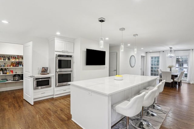 kitchen with white cabinetry, a center island, a kitchen bar, decorative light fixtures, and stainless steel double oven