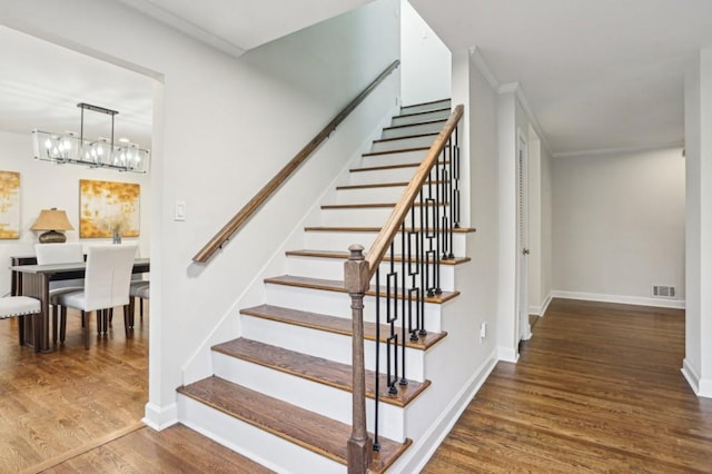 staircase featuring an inviting chandelier, wood-type flooring, and ornamental molding