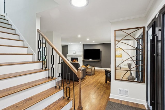 staircase featuring crown molding, a fireplace, and hardwood / wood-style flooring